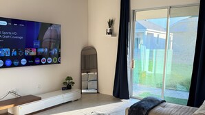 Un salon moderne doté d’un téléviseur à écran plat, d’un canapé, d’un tapis moelleux et d’une porte-fenêtre coulissante donnant sur un jardin.