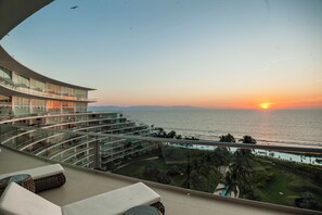 Un hotel moderno con un balcone curvo che si affaccia su un tramonto sull'oceano.