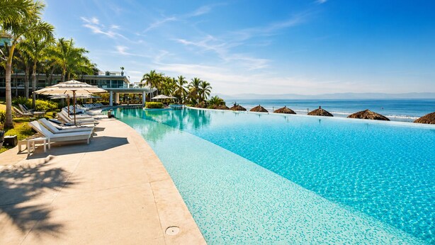A clear blue pool with lounge chairs and umbrellas, a building in the background, and a view of the ocean. - Beachfront Apartment | 6 Bedrooms | Nuevo Vallarta Peninsula (Bucerías)