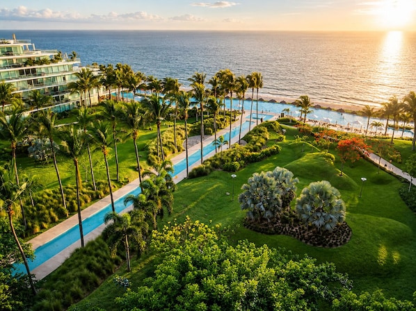 A resort with a swimming pool, palm trees, and a view of the ocean.