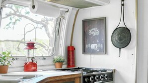 Une cuisine compacte équipée d’une cuisinière, d’un évier et d’une fenêtre donnant sur un espace verdoyant.