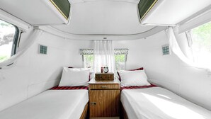 Un intérieur de camping-car compact comprenant deux lits, un espace de rangement central et une petite fenêtre avec des rideaux.