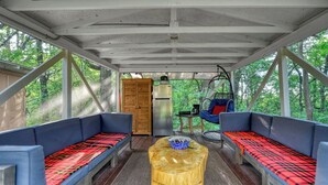 A covered outdoor seating area with two blue cushioned benches, a wooden table, and a hanging chair.