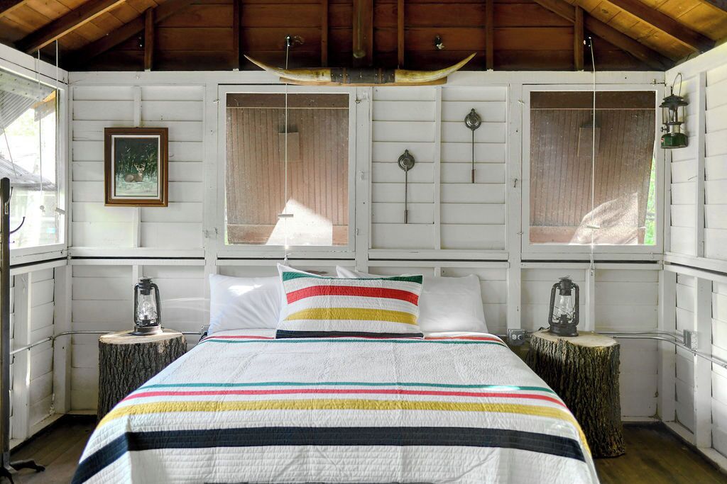 A bedroom with a bed, striped bedding, two lanterns, and wooden walls.