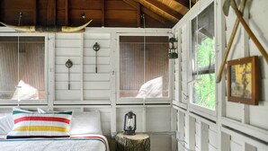 Ein rustikales Blockhütten-Zimmer mit Bett, Laterne und Fenster mit Blick auf grüne Landschaft.