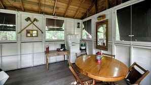 Eine rustikale Holzhütte mit Esstisch, Stühlen, einem Kühlschrank und einem Fenster mit Blick auf Bäume.