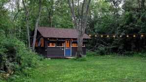 Eine rustikale Holzhütte, umgeben von dichtem Wald, mit einer Veranda und Lichterketten.