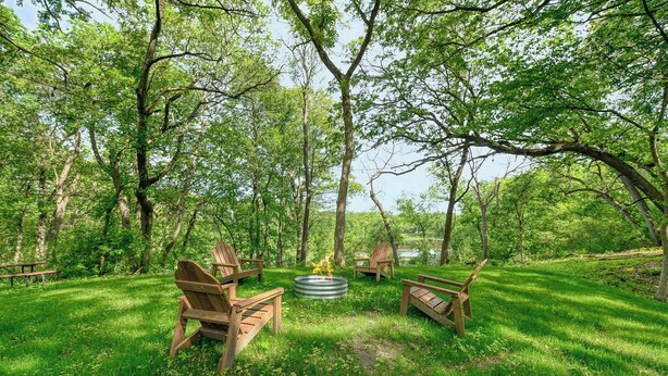 Ein Sitzbereich im Freien mit Holzbänken und einem Feuerkorb, umgeben von üppiger Vegetation und Bäumen.