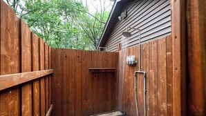 A wooden fenced outdoor shower area with a built-in showerhead and a small shelf. - Sun View - Antique Scout Cabin Suite (Troy)