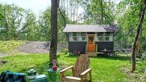 A small cabin with a wooden door, a picnic table, and a fire pit in a grassy area surrounded by trees. - Sun View - Antique Scout Cabin Suite (Troy)