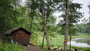 Una cabaña rústica con fachada de madera, un porche y una hamaca junto a un lago.