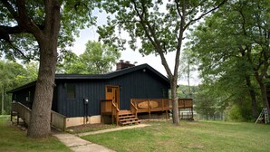 Une cabane en bois avec une véranda, une cheminée et une petite terrasse.