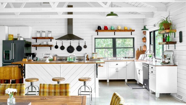 Une cuisine moderne avec des meubles blancs, un îlot central en bois et des ustensiles de cuisine suspendus.