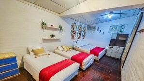 Habitación de hotel con tres camas, un armario, ventilador de techo y adornos en las paredes.