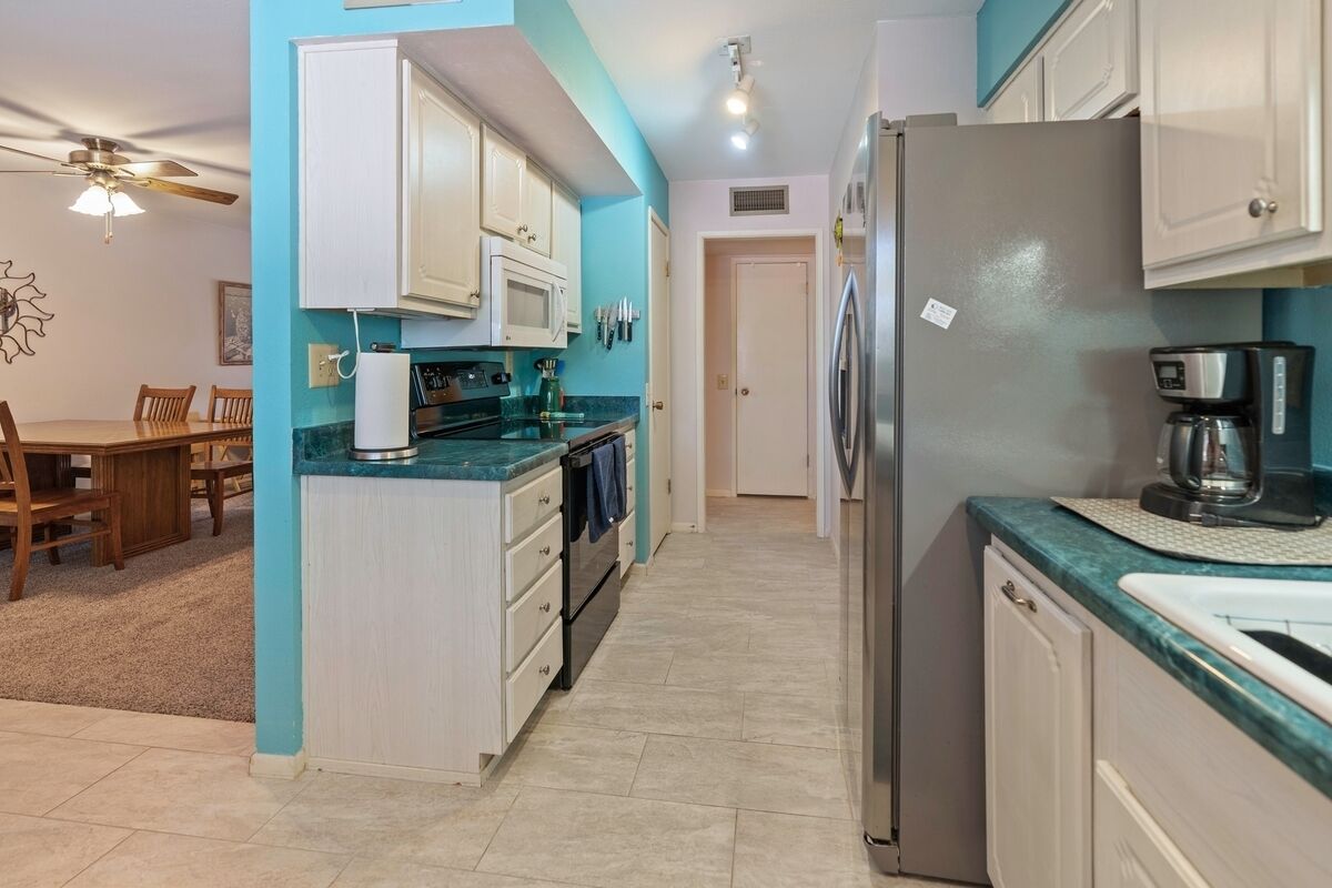 Una cocina compacta con armarios blancos, un refrigerador de acero inoxidable y una cafetera.