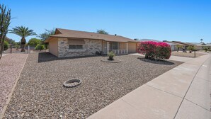 A single-story house with a stone facade, a front porch, and a small garden area with a palm tree and a flowering bush. - Pet-Friendly Sun City Retreat Near Golf & Shops (Sun City)