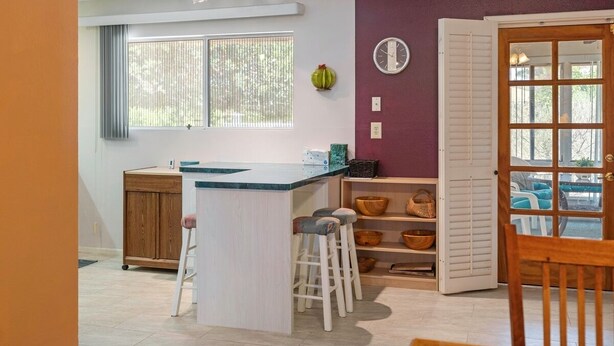 A kitchen with a central island, stools, a wooden cabinet, and a window with blinds. - Pet-Friendly Sun City Retreat Near Golf & Shops (Sun City)
