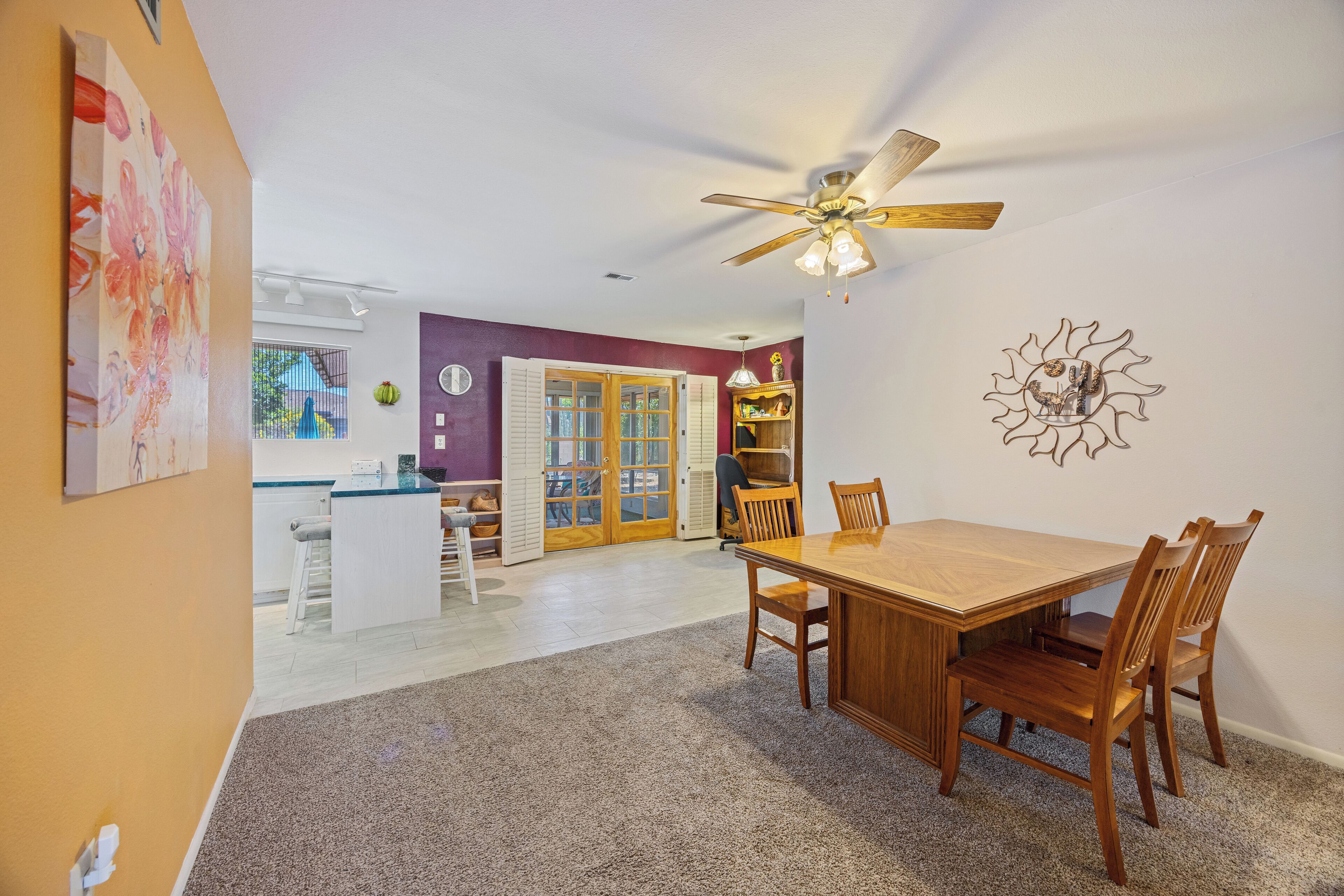 A dining area with a wooden table and chairs, a ceiling fan, and a kitchen in the background.