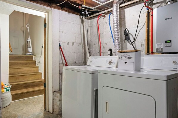 A laundry room with two stacked washers and dryers, a water heater, and visible plumbing. - Cozy Mid-Century Home / Hot Tub • Game Room • Sleeps 14 (Oak Hill)