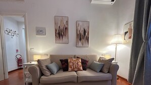 A living room with a beige sofa, two wall-mounted abstract paintings, a fire extinguisher, and a lamp on a side table. - Domus Vittoria, the ideal apartment for your family in the Vatican area (Roma)