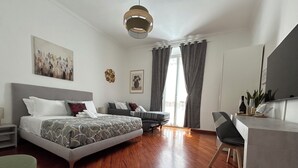 A modern hotel room with a large bed, a desk, and a chair. There is a window with curtains, a painting on the wall, and a ceiling light. - Domus Vittoria, the ideal apartment for your family in the Vatican area (Roma)
