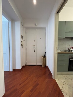 A hallway with wooden flooring leading to a white door with a keyhole and a small window. - Domus Vittoria, the ideal apartment for your family in the Vatican area (Roma)