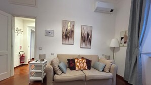 A living room with a beige sofa, two side tables, a fire extinguisher, and abstract wall art. - Domus Vittoria, the ideal apartment for your family in the Vatican area (Roma)