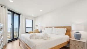 A spacious bedroom with a large bed, a wooden headboard, and a view of the beach through a sliding glass door. - Stunning Ocean Views, Steps from Beach, Modern/Updated Condo- 302 Summerhouse (Isle Of Palms)