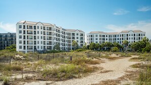 A modern multi-story hotel with a flat roof and balconies, surrounded by a sandy beach and sparse vegetation. - Stunning Ocean Views, Steps from Beach, Modern/Updated Condo- 302 Summerhouse (Isle Of Palms)