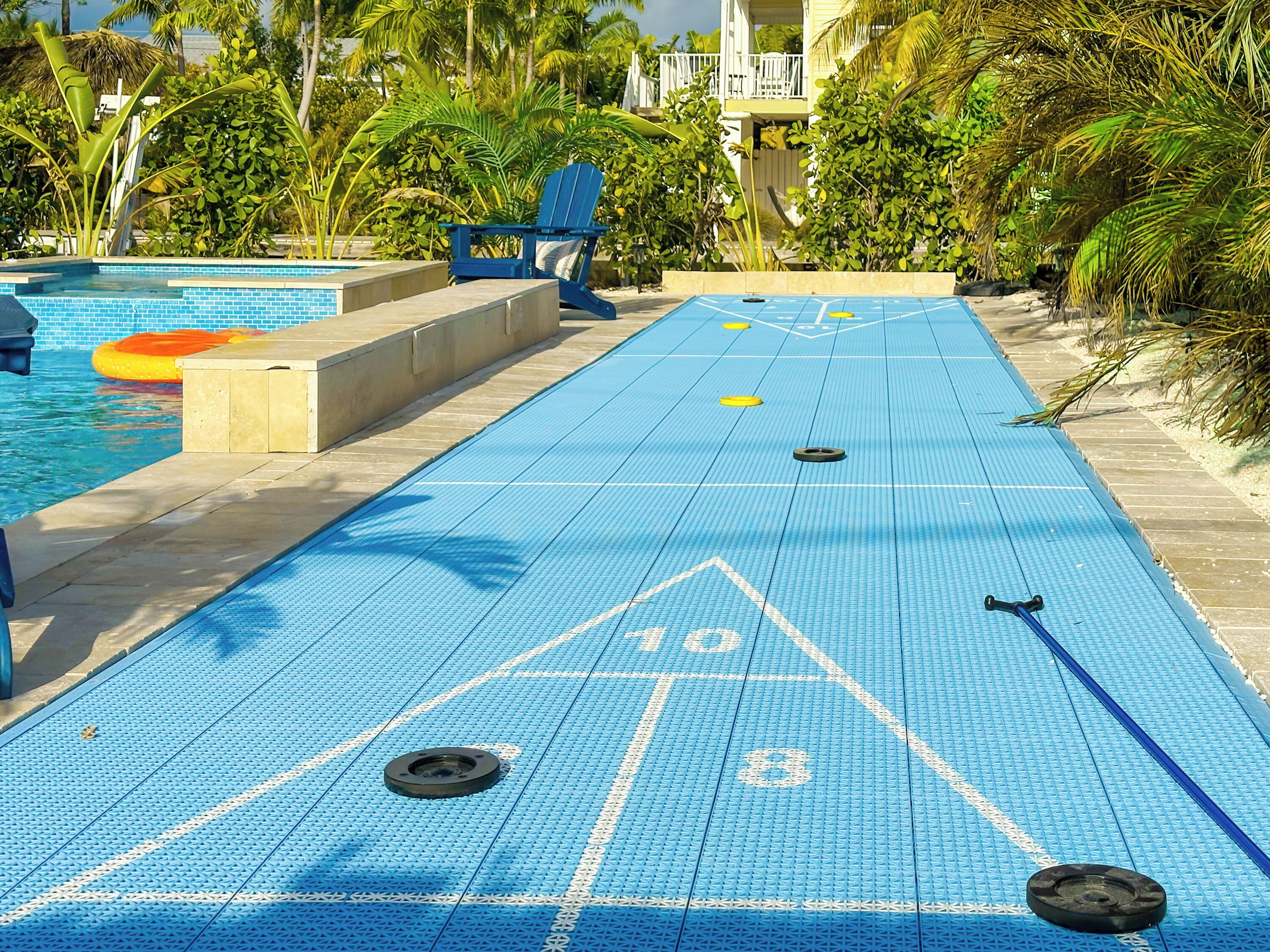 Una taula de shuffleboard amb superfície blava, una piscina i una cadira blava.