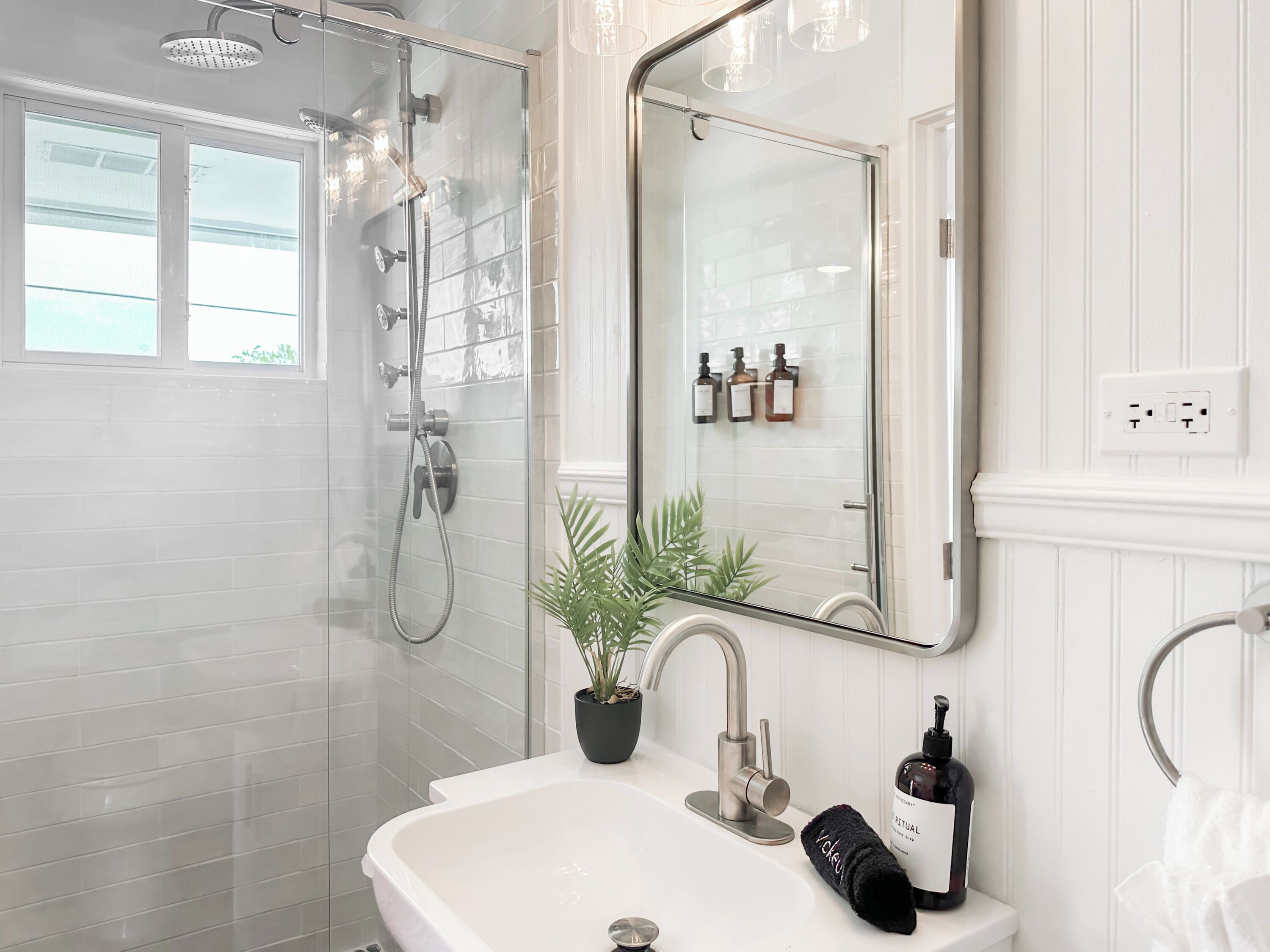 A modern bathroom with a glass-enclosed shower, a white sink, and a mirror above it.