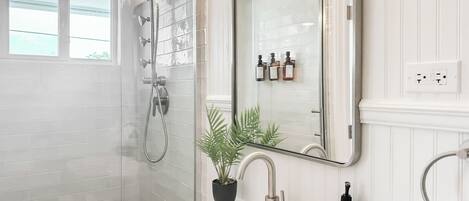 A modern bathroom with a glass-enclosed shower, a white sink, and a mirror above it.