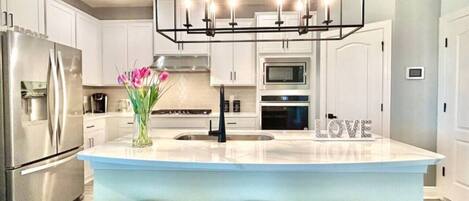 A modern kitchen with a central island, stainless steel appliances, and a decorative 'LOVE' sign.