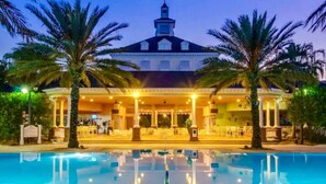 Ein Hotel mit Pool, Palmen und einem überdachten Außenbereich mit Sitzgelegenheiten.