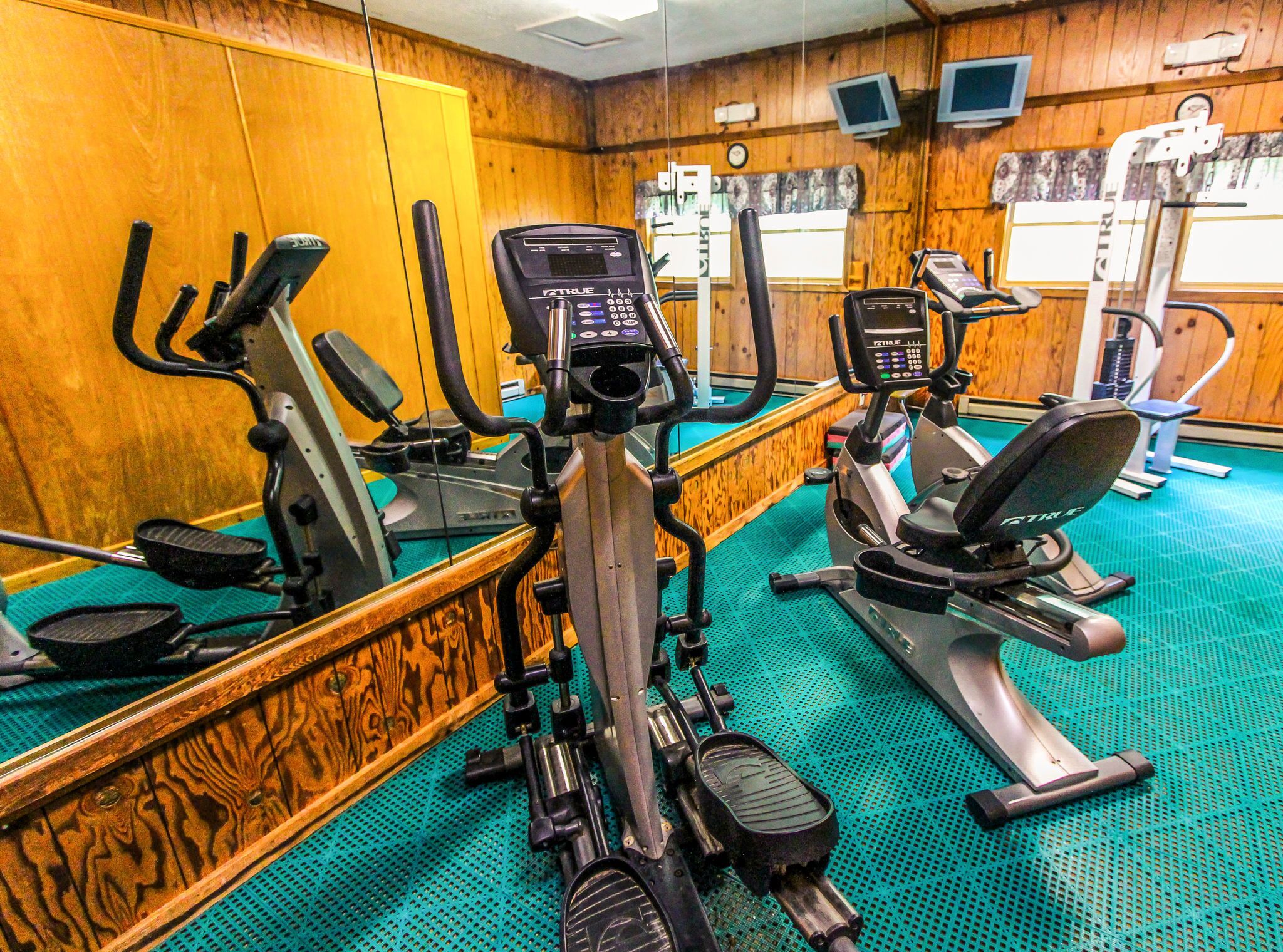 A gym with cardio machines, mirrors, and wooden walls.
