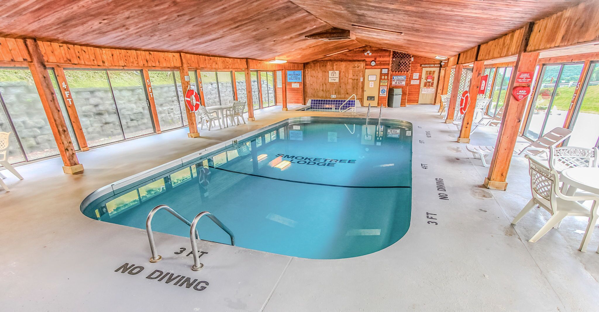 Une piscine intérieure avec un panneau indiquant « Il est interdit de plonger », entourée de murs en bois et dotée de grandes fenêtres.