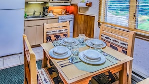 Una cocina compacta con una mesa de comedor dispuesta para cuatro personas, sillas de madera con diseños de animales, un microondas, una estufa y una ventana con persianas.