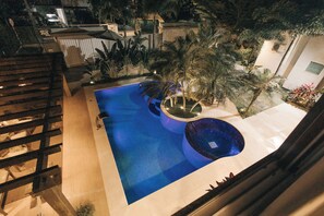 A rooftop pool with a blue water feature, surrounded by palm trees and a wooden deck. - JARDIM DO RIO SUÍTES (Florianopolis)
