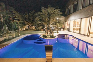 A swimming pool with a fountain, surrounded by palm trees and a building with large windows. - JARDIM DO RIO SUÍTES (Florianopolis)