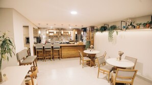 A modern kitchen with wooden cabinets, a central island, and pendant lighting. There is a dining area with a round table and chairs. - JARDIM DO RIO SUÍTES (Florianopolis)
