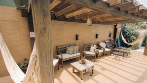 A covered outdoor seating area with wooden furniture, a hammock, and a potted plant. - JARDIM DO RIO SUÍTES (Florianopolis)
