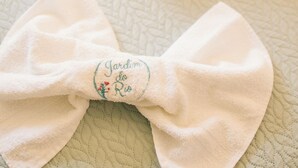 A bed with a quilted white bedspread and two neatly folded white towels. - JARDIM DO RIO SUÍTES (Florianopolis)