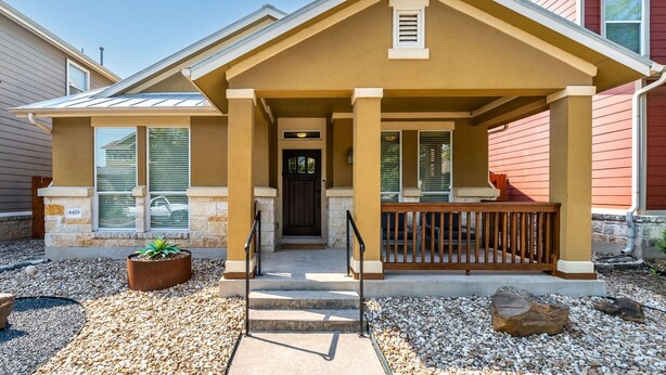A two-story house with a covered porch, a front door, and a small garden area with pebbles and a potted plant. - One-Story 3BR/3BA Home - Central Austin - Mueller Neighborhood (Austin)