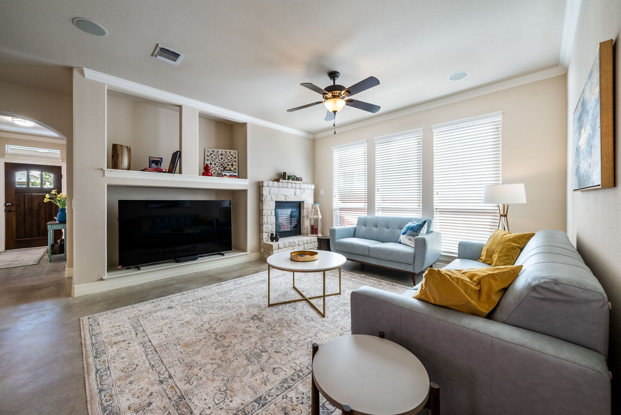 A living room with a fireplace, a ceiling fan, and a large flat-screen TV.