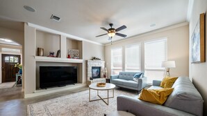 A living room with a fireplace, a ceiling fan, and a large flat-screen TV. - One-Story 3BR/3BA Home - Central Austin - Mueller Neighborhood (Austin)
