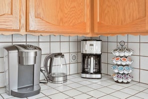 Een keuken met een koffiezetapparaat, een waterkoker en een bekerhouder.