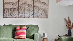 A green sofa with a striped pillow, a small round wooden table with a candle, and a decorative vase with dried plants.