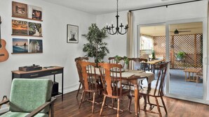 Un comedor con una mesa y sillas de madera, una araña y una guitarra en la pared.