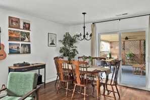 Een eethoek met een houten tafel en stoelen, een kroonluchter en een gitaar aan de wand.
