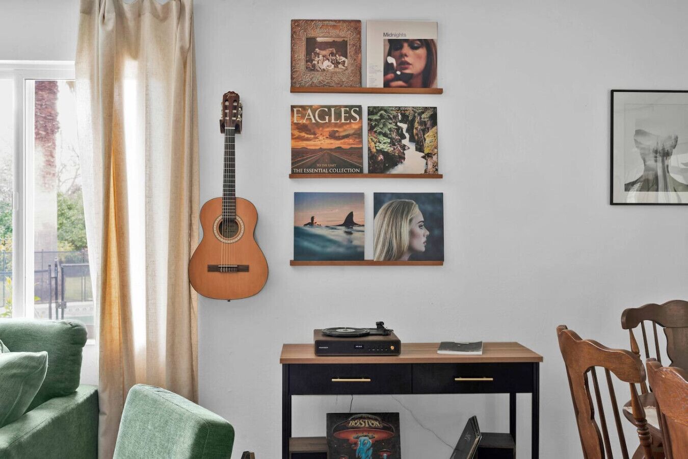 Une pièce avec une guitare, un mur orné de tableaux, une table avec un tourne-disque et une chaise.